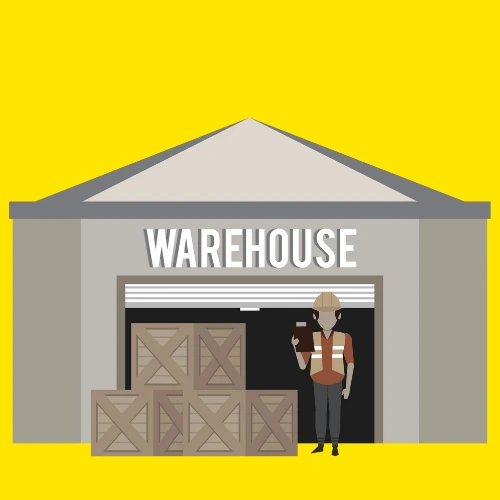 A worker in a safety vest stands outside a warehouse with stacked boxes.